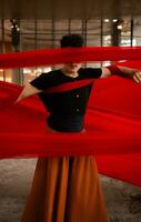 an Asian man standing proudly among the red cloth that dangles in an old building photo