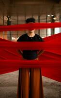 an Asian man standing proudly among the red cloth that dangles in an old building photo