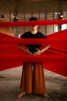 an Asian man standing proudly among the red cloth that dangles in an old building photo