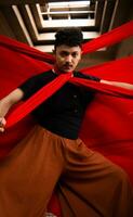an Asian man in a black shirt is strangled with a red cloth while standing in an old building against a red background photo