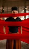 an Asian man standing proudly among the red cloth that dangles in an old building photo