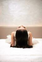 an Asian woman with black hair is sleeping on a white bed in an elegant hotel photo