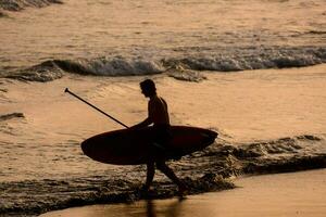 a man carrying a surfboard on the beach at sunset photo