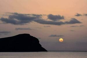 the sun setting over the ocean with a small island in the background photo