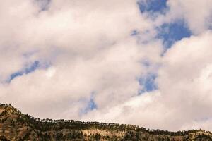 a mountain with trees on top and clouds in the sky photo