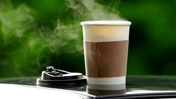 coffee takeaway in a paper cup on top of the car roof green tree background at sunrise in the morning,  selective focus, soft focus. video