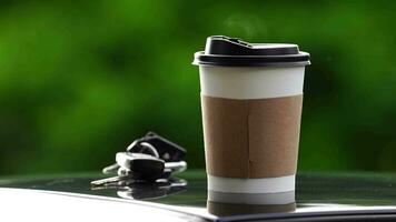 coffee takeaway in a paper cup on top of the car roof green tree background at sunrise in the morning,  selective focus, soft focus. video