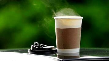 coffee takeaway in a paper cup on top of the car roof green tree background at sunrise in the morning,  selective focus, soft focus. video