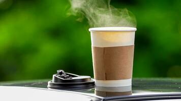 café para llevar en un papel taza en parte superior de el coche techo verde árbol antecedentes a amanecer en el mañana, selectivo enfocar, suave enfocar. foto