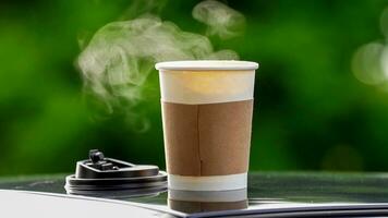 café para llevar en un papel taza en parte superior de el coche techo verde árbol antecedentes a amanecer en el mañana, selectivo enfocar, suave enfocar. foto