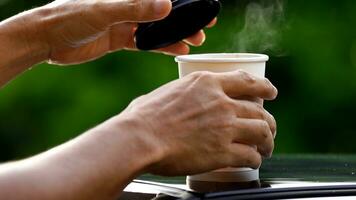 café para llevar en un papel taza en parte superior de el coche techo verde árbol antecedentes a amanecer en el mañana, selectivo enfocar, suave enfocar. foto