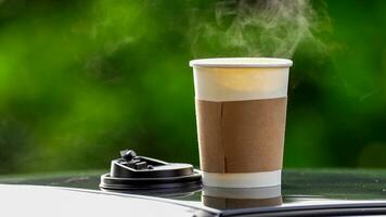 café para llevar en un papel taza en parte superior de el coche techo verde árbol antecedentes a amanecer en el mañana, selectivo enfocar, suave enfocar. foto
