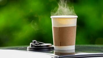 coffee takeaway in a paper cup on top of the car roof green tree background at sunrise in the morning,  selective focus, soft focus. photo