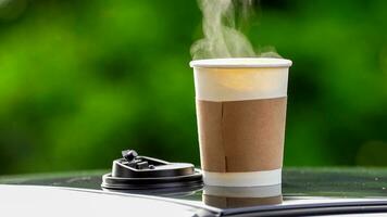 coffee takeaway in a paper cup on top of the car roof green tree background at sunrise in the morning,  selective focus, soft focus. photo