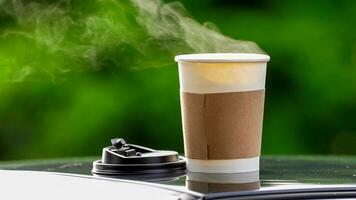 coffee takeaway in a paper cup on top of the car roof green tree background at sunrise in the morning,  selective focus, soft focus. photo