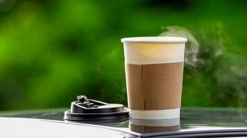 coffee takeaway in a paper cup on top of the car roof green tree background at sunrise in the morning,  selective focus, soft focus. photo