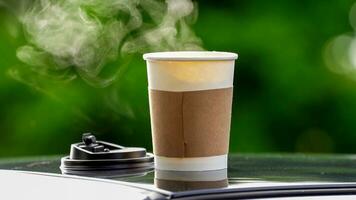 coffee takeaway in a paper cup on top of the car roof green tree background at sunrise in the morning,  selective focus, soft focus. photo