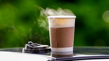 coffee takeaway in a paper cup on top of the car roof green tree background at sunrise in the morning,  selective focus, soft focus. photo