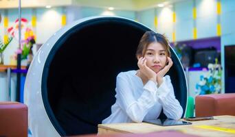 Beautiful asian business woman is sitting on a modern round chair with sad face on the table has a phone and tablet on it while looking at the camera,Copy space, Digital marketing. photo