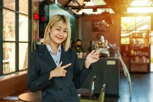 With a proud smile, the beautiful business girl pointed to her cafe and enthusiastically invited passersby to come in and check it out. photo