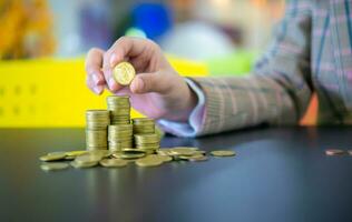 A hand that is about to place coin to the pile of gold coins on the black table, Finance and management concept, Concept of saving money for the future. photo