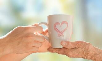 The hands of a young man serve a cup to the hands of an elderly woman. Care concept. photo