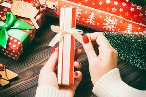 Top view of female hand tie up New Year present on festive wooden background. Fir tree and holiday decorations. Christmas time concept photo