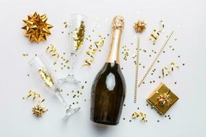 Bottle of champagne with colored glitter, confetti and gift box space for text on colorfull background, top view. Hilarious, christmas and birthday celebration photo