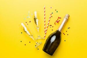 bottle of champagne with glasses and colorful confetti on colored background. top view flay lay photo