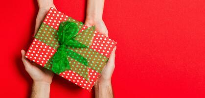 Top view of holding a gift in female and male hands on colorful background. Woman and man give and receive a present. Time for holiday concept with copy space photo