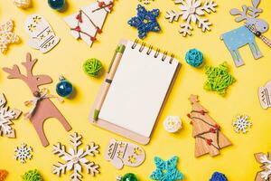 Top view of notebook on yellow background with New Year toys and decorations. Christmas time concept photo