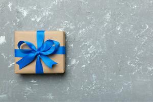 Holiday gift box wrapped in craft paper with colored bow on table background. Top view, flat lay, copy space photo