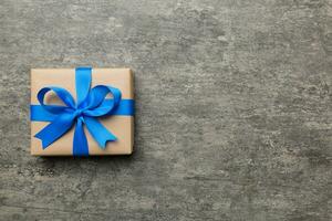 Holiday gift box wrapped in craft paper with colored bow on table background. Top view, flat lay, copy space photo