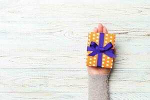 Woman hands give wrapped christmas or other holiday handmade present in colored paper . Present box, decoration of gift on white rustic wooden table, top view with copy space photo