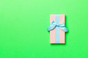 wrapped Christmas or other holiday handmade present in paper with blue ribbon on green background. Present box, decoration of gift on colored table, top view with copy space photo