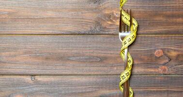 Top view of wrapped fork in tape measure on wooden background. Healthy eating and diet concept photo