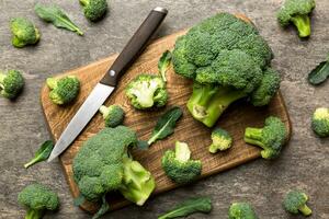 fresh green broccoli on wooden cutting board with knife. Broccoli cabbage leaves. light background. Flat lay photo