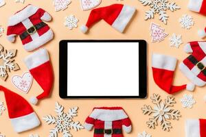 Top view of digital tablet with Christmas decorations and Santa hats on orange background. Happy holiday concept photo