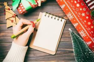 Top view of female hand writing in a notebook on wooden Christmas background. Fir tree and festive decorations. Wish list. New Year concept photo