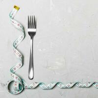 Composition of curled measuring tape and fork on cement background with empty space for your design. Overweight concept photo