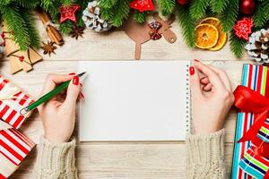 vista superior de la mano femenina escribiendo en un cuaderno sobre fondo de Navidad de madera. abeto y decoraciones festivas. lista de deseos concepto de año nuevo foto