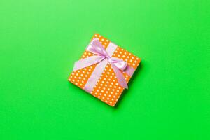 wrapped Christmas or other holiday handmade present in paper with pink ribbon on green background. Present box, decoration of gift on colored table, top view with copy space photo