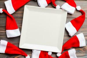 Festive set of plate decorated with Santa Claus hat on wooden background. Top view christmas dinner concept photo