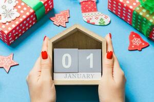 vista superior de las manos femeninas sosteniendo el calendario sobre fondo azul. el primero de enero. decoraciones navideñas. concepto de año nuevo foto