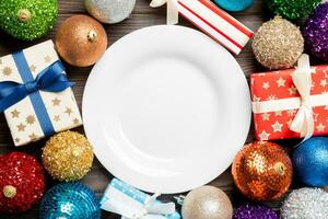 Top view of holiday setting on wooden background. Plate, gifts, baubles and Christmas decorations. New Year dinner concept photo