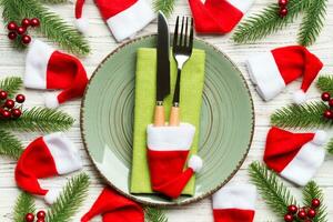 Holiday composition of plate and flatware decorated with Santa hat on wooden background. Top view of Christmas decorations. Festive time concept photo
