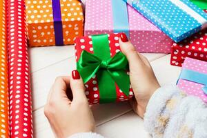 vista superior de la mano femenina atar regalo de año nuevo sobre fondo de madera festiva. cajas de regalo y papel de regalo enrollado. concepto de tiempo de navidad foto