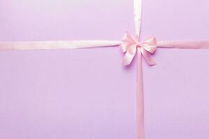 Top view of purple ribbon rolled and pink bow isolated on colored background. Flat lay with copy space photo