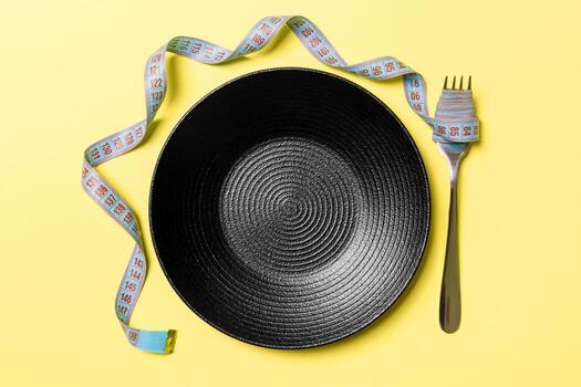 Strict diet concept with empty space fro your design. Top view of plate with fork in measuring tape on orange background photo