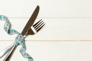 Composition of curled wrapped measuring tape, fork and knife on wooden background with empty space for your design. Overweight concept photo